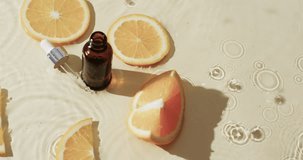 Video of beauty product bottle, pipette, orange slices in water with copy space on yellow background. Health and beauty, make up, beauty products, colour and movement concept.