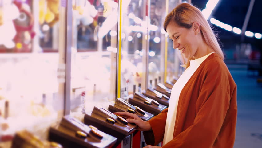 Girl plaing claw machine on a fun fair amusiment park. Night fair illumination, Ferris wheel spinning in the background. Fun for the whole family