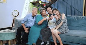 Happy Indian excited family sitting on sofa smiling teenage boy hold smartphone taking selfie at house. Old aged grandparents couple make funny pose photo or record video blog enjoy weekend together