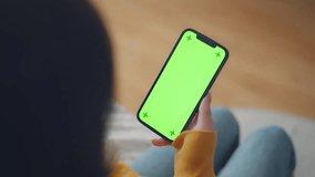 Hand of woman holding mobile smartphone and swipes photos or pictures with blank green screen mock up while sitting on a sofa at home, Chroma key mock-up on smartphone in hand - Powered by Shutterstock - Get 15% off with code: PIKWIZARD15