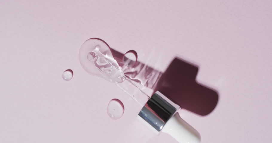 Vertical video of make up pipette and drops of serum with copy space on pink background. Health and beauty, make up, beauty products, colour and movement concept.