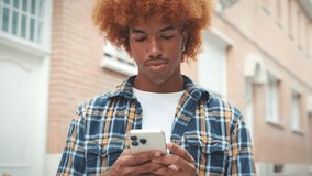 Guy with an African hairstyle wearing blue shirt uses mobile phone outside on the street - Powered by Shutterstock - Get 15% off with code: PIKWIZARD15
