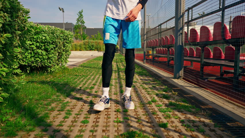 tall guy basketball player walks down the park path to the basketball court and drives the ball showing off his dribbling skills