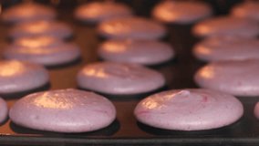 Video in time-lapse showing the baking of homemade purple macaroon cookies in the oven, with a close-up macro perspective as they expand.