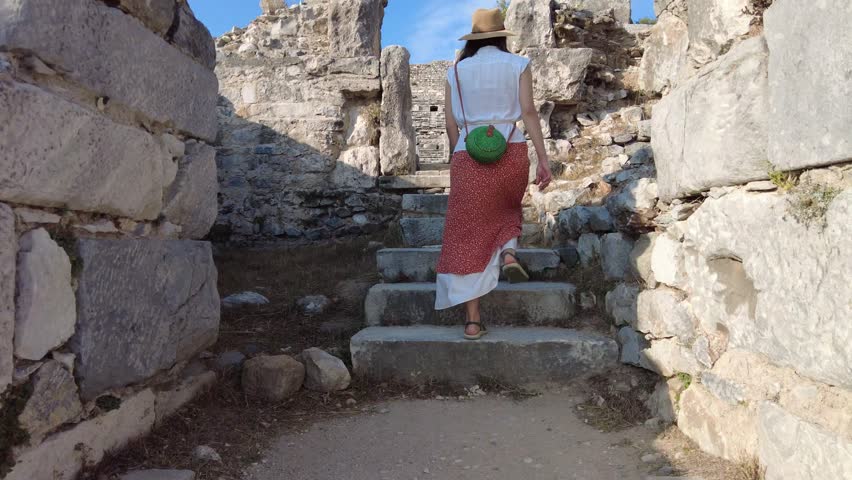 Young woman walk in ancient greek city on the western coast of Anatolia, look on antique amphitheater. Ancient theatre of Miletus, Didim, Aydın, Türkiye
