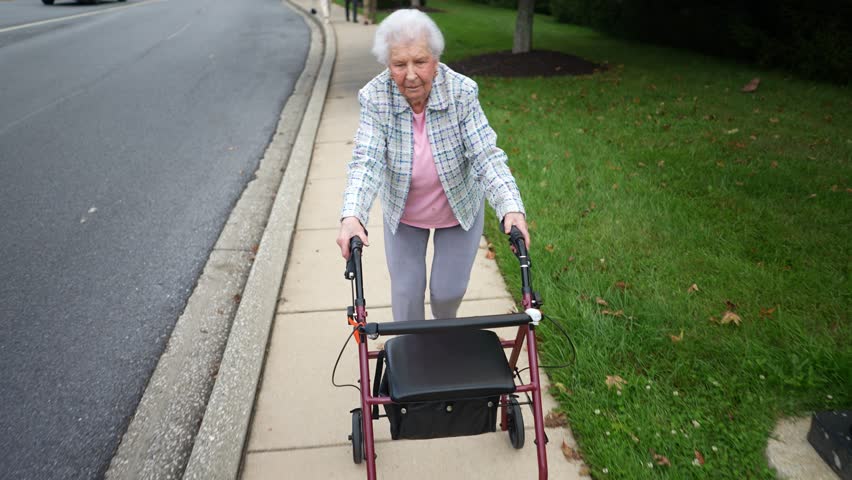 Front view of elderly senior old woman using walker for mobility on sidewalk for a walk. Concept of elderly independence.