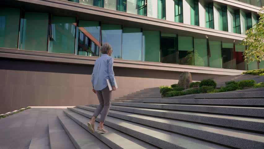 Back view businesswoman middle-aged lady manager CEO entrepreneur leader professional lawyer unrecognizable woman walking outdoors to office building city business center walk up stairs climbing steps