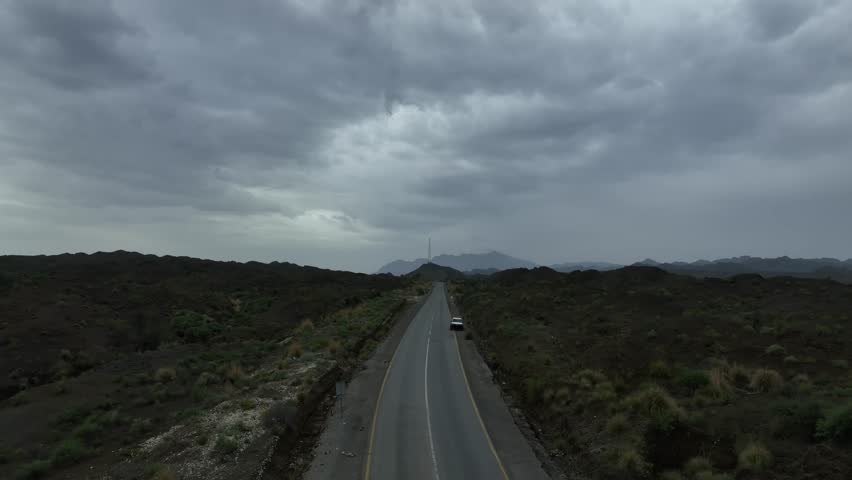 Aerial drone shot of a highway with a vehicle moving on the road and wast landscape and dark clouds on the sky