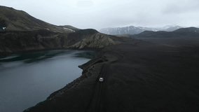 Aerial view from a 4x4 car driving around the Blahylur crater lake in Southern Highlands of Iceland during summer. Incredible greys and greens landscape in an empty brown road.