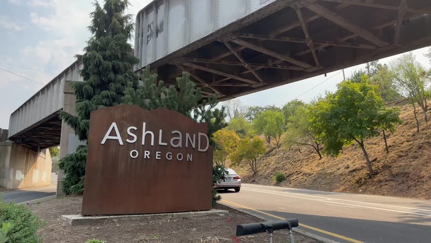 Cars passing the sign welcoming people to Ashland, Oregon.
