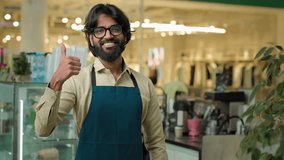Coffee shop worker show like agree recommend gesture approve hand symbol successful happy smiling cafe waiter guy Indian Arabian male cafeteria working showing thumb up barista man small business - Powered by Shutterstock - Get 15% off with code: PIKWIZARD15