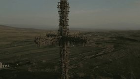 The largest iron cross in Armenia in the rays of the setting sun. On the background of high mountain Aragats in clear weather. Drone video. Close-up, the camera moves in an arc.
