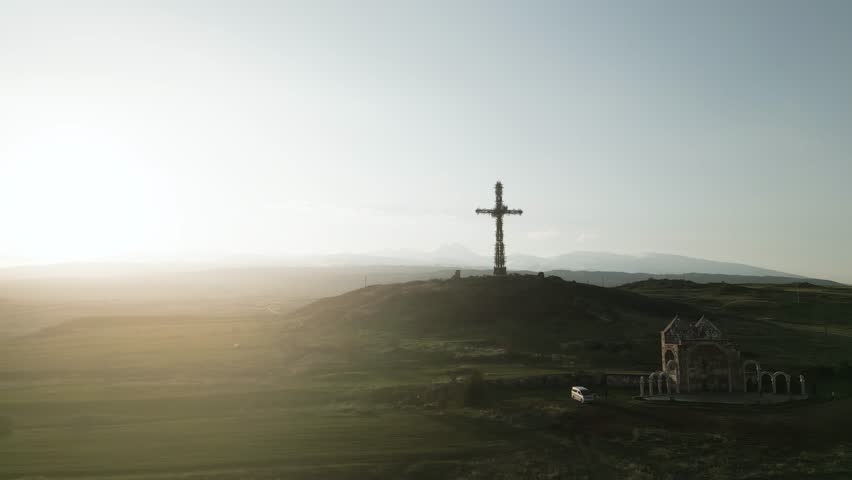 The largest iron cross in Armenia in the rays of the setting sun. On the background of high mountain Aragats in clear weather. Drone video. Distant plan, the camera moves in an arc. Royalty-Free Stock Footage #1109721309