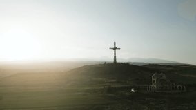 The largest iron cross in Armenia in the rays of the setting sun. On the background of high mountain Aragats in clear weather. Drone video. Distant plan, the camera moves in an arc.