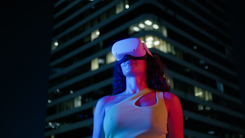 Young woman uses virtual or augmented reality helmet in magic atmosphere of blue neon light in urban futuristic city background. Female VR headset user of digital interactive app, entertainment future Royalty-Free Stock Footage #1109726217