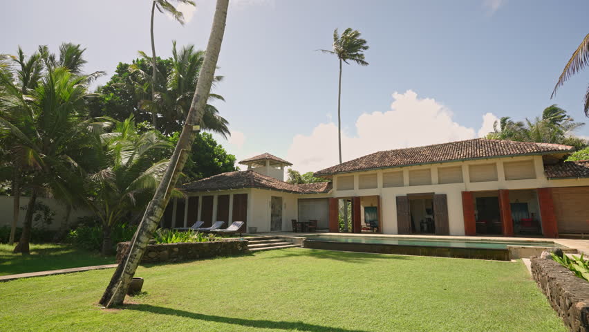 Giant luxury tourist retro villa for rent during summer vacation on tropical island beach. Antique resort house with vintage furniture, swimming pool and palm trees on backyard at coastline.