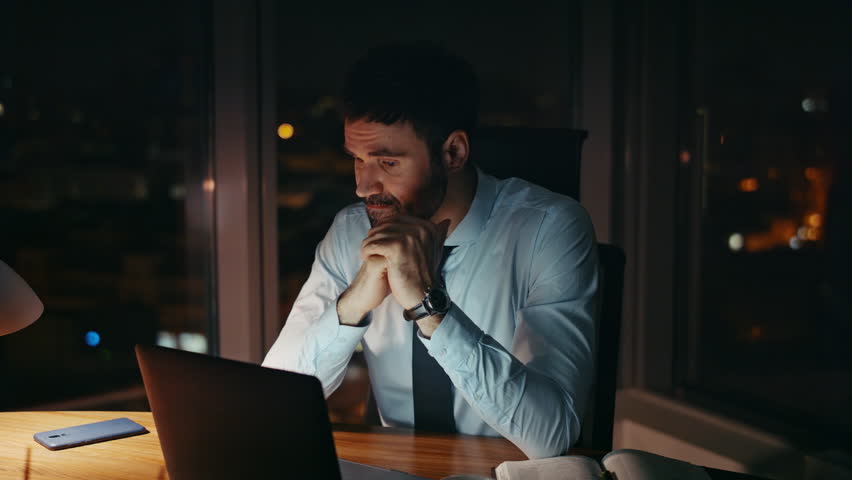 Unhappy manager sitting at dark office looking laptop monitor close up. Sad analyst working overtime with computer reports late evening. Anxious businessman worried job problems feeling tired at night | Shutterstock HD Video #1109730855