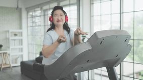 Happy Asian senior woman jogging and listening to music on treadmill at home. - Powered by Shutterstock - Get 15% off with code: PIKWIZARD15