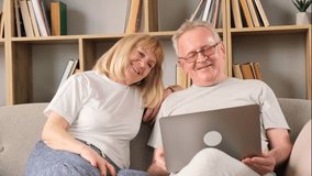 Happy middle-aged couple chatting online at home using laptop.