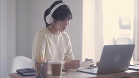 young university students Asian women using laptop wearing headphone, taking notes online elearning class webinars, online web education concept.