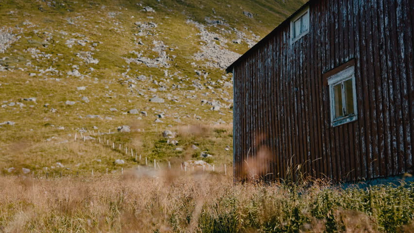 A weathered red barn set against the dramatic backdrop of a grass-covered mountain slope