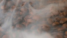 Slow motion of roasted coffee beans falling with smoke. Organic coffee seeds.