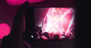 Closeup, phone screen filming band concert. Girl holding phone camera in hands at rock band concert. Pink magenta bright spotlights flashing in stage. Audience at festival event. Disco entertainment