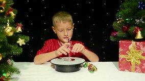On a black background with flashing lights, a boy decorates a small Christmas tree with small toys