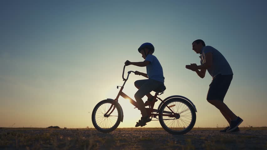 family play in the park. father teaching son to ride a bike. happy family kid dream concept. son learn to ride bike silhouette sunset. father supporting child son riding bike summer in the park Royalty-Free Stock Footage #1109741959