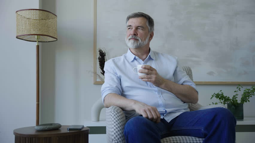 Portrait of handsome mature man take sip drinking hot tea or coffee while sitting on couch at home. Calm relaxed male enjoying weekend leisure time alone indoors | Shutterstock HD Video #1109744741