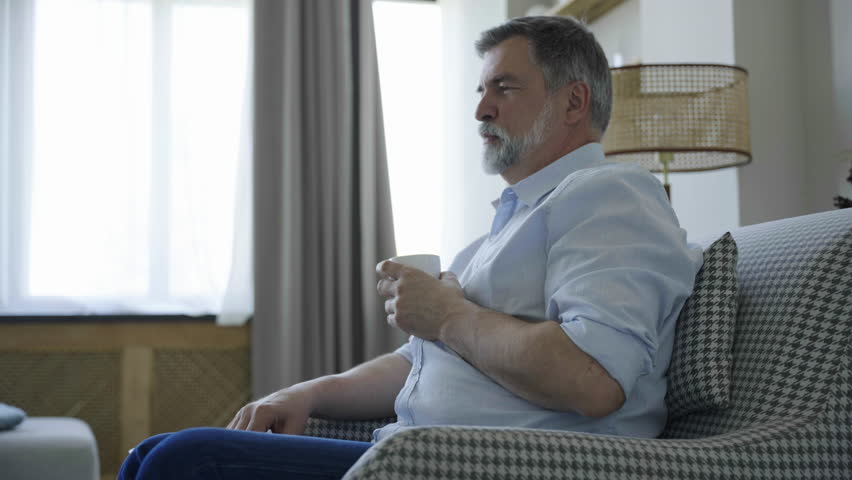 Portrait of handsome mature man take sip drinking hot tea or coffee while talking with somebody at home. | Shutterstock HD Video #1109744745