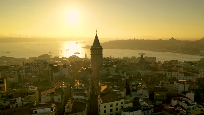 Aerial view of Istanbul at sunset from a drone orbiting the Galata Tower. There are many residences around the Galata Tower, with the Golden Horn waterway in the background.