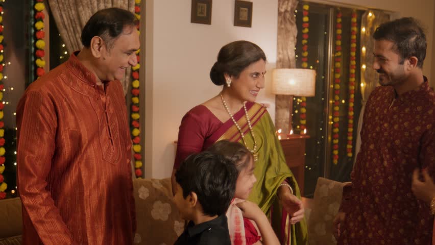 Happy smiling Hindu ethnic Indian family in traditional attire greeting each other and celebrating the religious occasion of Diwali festival indoors in decorated house with lights and flower garlands Royalty-Free Stock Footage #1109746283