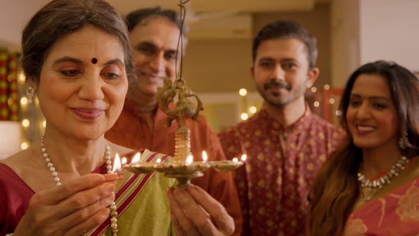 Happy smiling Hindu ethnic Indian family group members lighting up traditional diyas or oil lamps on the auspicious occasion of Diwali festival in decorated home. Festive season, relationship concept. Royalty-Free Stock Footage #1109746435