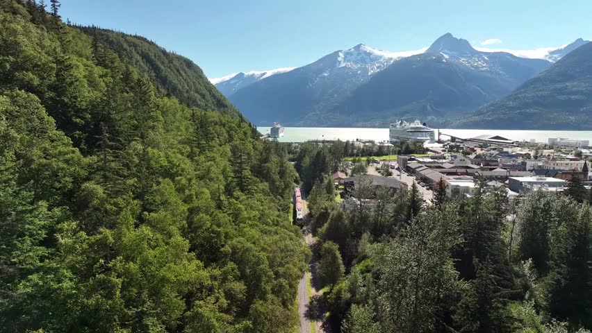 An aerial view of a train passing a mountain landscape and city under a bright sunny day