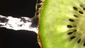 Creative layout of sliced kiwi and water. Splashes on black background. Freshly sliced kiwi splashes in cold water in insulation. Concept of healthy eating and freshness. Slow motion. Vertical video