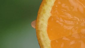 Drops of juice or water close-up drop from slice of ripe orange. Concept of fresh vegetables and fruits. Orange with dripping clear juice on green background. slow motion. vertical video