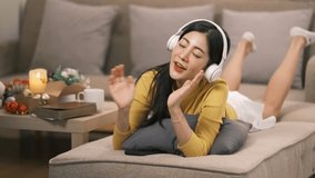 Smiling woman with headphones listening to music, relaxing on sofa in Christmas living room - Powered by Shutterstock - Get 15% off with code: PIKWIZARD15