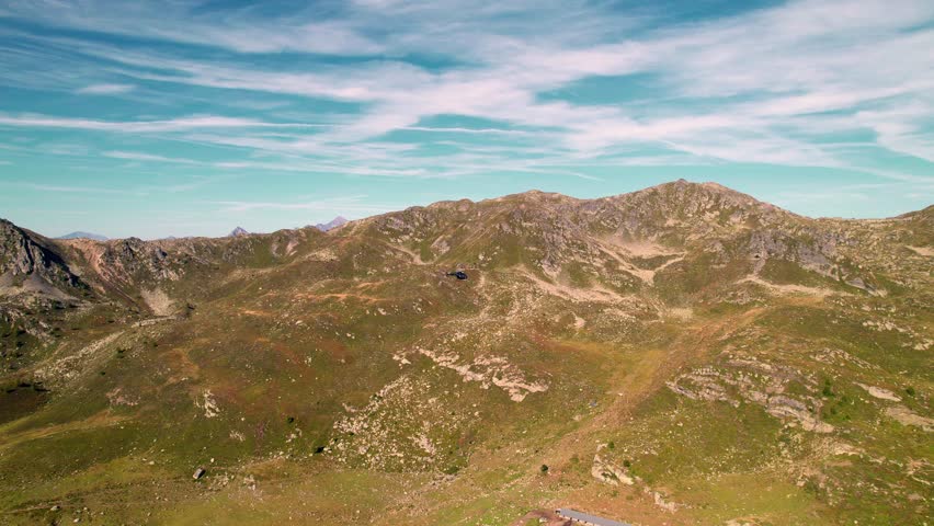A helicopter flying over a range of hiking mountains with cloudy blue sky on the horizon