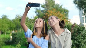 Happy sisters watching a video, taking a selfie on a smartphone outdoors in the park. Childhood.