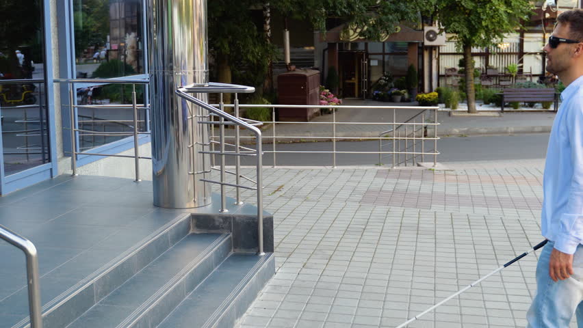 A blind man with walking stick enters the steps in the building