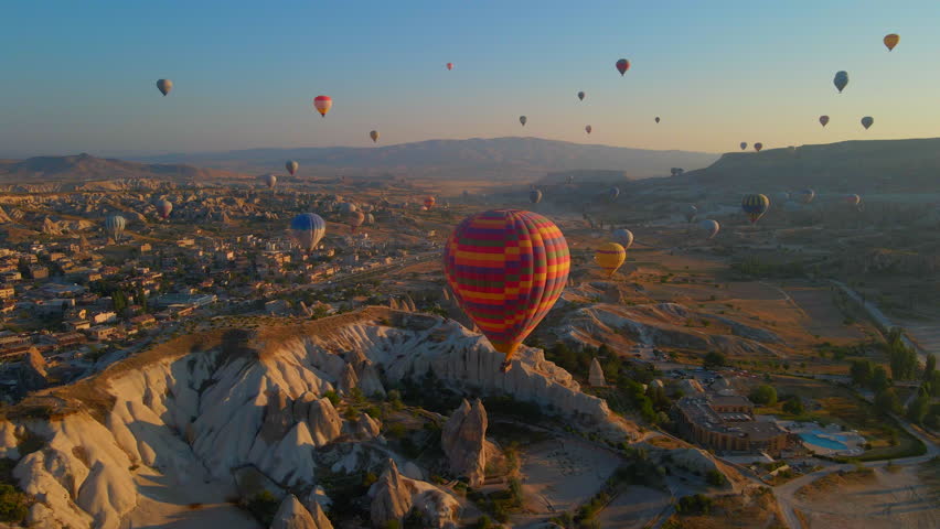 In this aerial video, the skies above Cappadocia, Turkey, come alive with a kaleidoscope of hot air balloons. Against the backdrop of the region's iconic valleys, rocks, and fields, this mesmerizing Royalty-Free Stock Footage #1109770605