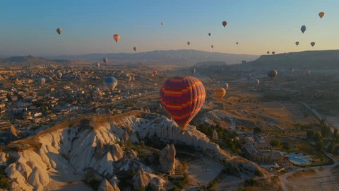 In this aerial video, the skies above Cappadocia, Turkey, come alive with a kaleidoscope of hot air balloons. Against the backdrop of the region's iconic valleys, rocks, and fields, this mesmerizing Arkistovideo