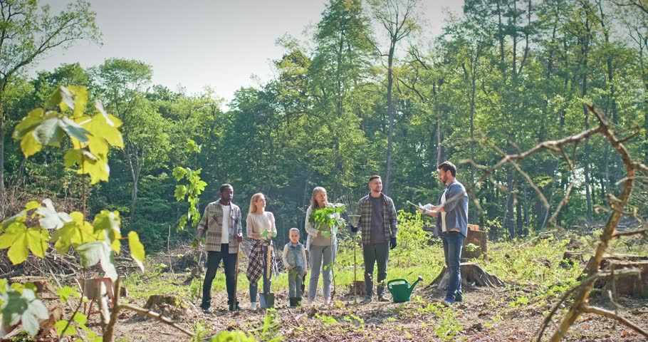 Side view of enthusiastic multicultural multiage group of people providing forestation for ecology. Happy volunteers listen to instructor and helping nature. Environment concept.