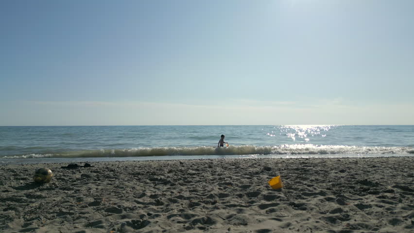 A young kid playing in the shallow water on a sandy beach on a sunny day