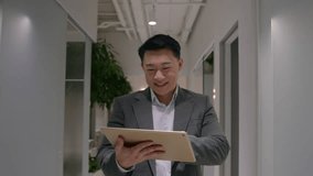 Smiling Asian businessman middle-aged happy chinese korean multiethnic man walking in office hallway corridor use digital tablet computer device browsing internet business social media going at lobby - Powered by Shutterstock - Get 15% off with code: PIKWIZARD15