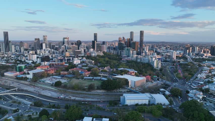 Establishing shot of Brisbane City and Brisbane Girls Grammar School from above Victoria Park Kelvin Grove. Camera drone orbiting around the Inner City Bypass in Foreground. Brisbane City Sunset