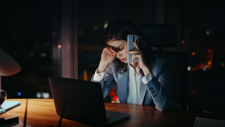Overwhelmed worker talking smartphone sitting office at night close up. Tired overworked business woman complaining at phone call working at laptop late evening. Displeased girl speaking telephone. Royalty-Free Stock Footage #1109780477