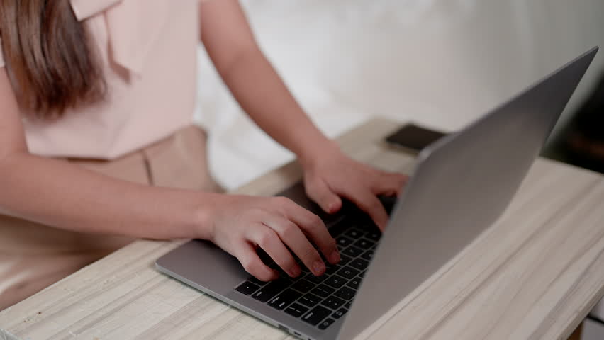 Close-up of the hand of an anonymous Asian woman with long hair. Sitting at home working on the bed. Typing with laptop keyboard, hands resting on computer, fingers pressing keyboard. Royalty-Free Stock Footage #1109788221
