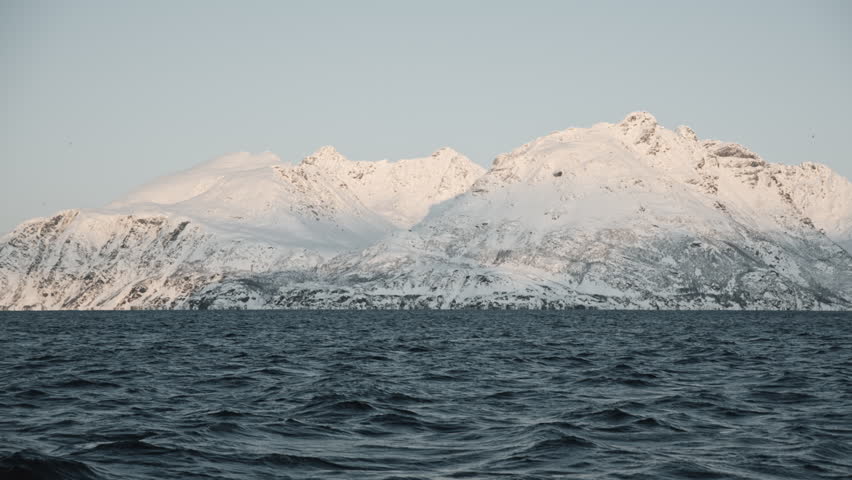 Cinematic Norway winter fjord landscape at picturesque sunset. Dark calm waves nobody in the sea. Nordic Scandinavian snowy coastline, Ice islands. Polar Norwegian mountains atmosphere. Arctic circle